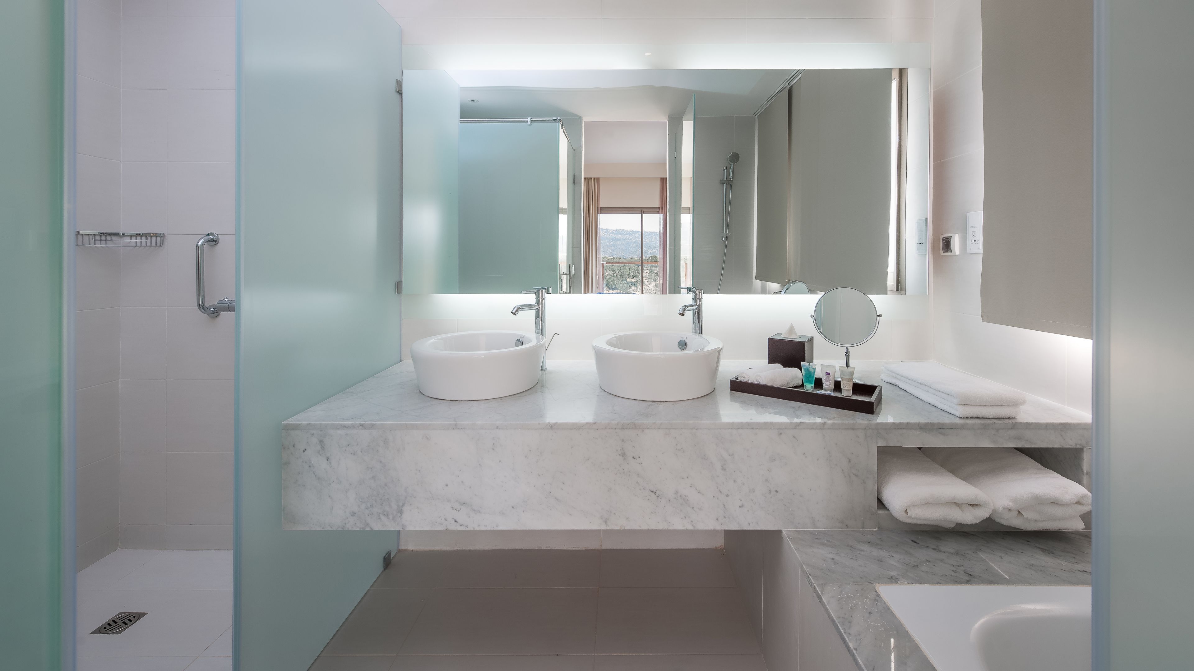 A modern bathroom with two sinks, a large mirror, and a bathtub.