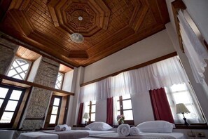 A hotel room with a wooden ceiling, large windows with curtains, and a bed with neatly rolled towels. - Kalemi Hotel (Gjirokastër)