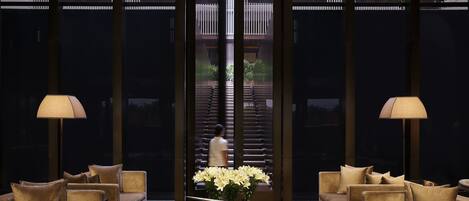 A modern lobby with a central coffee table, sofas, and a large window with blinds.