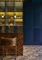 Zona de bar con estanterías llenas de botellas, luces colgantes y un suelo estampado.