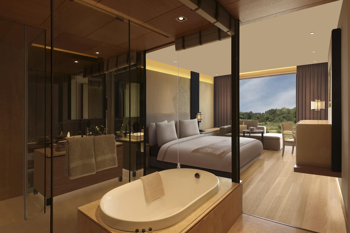 A modern bedroom with a large bed, a separate bathroom with a bathtub, and a view of the outdoors.