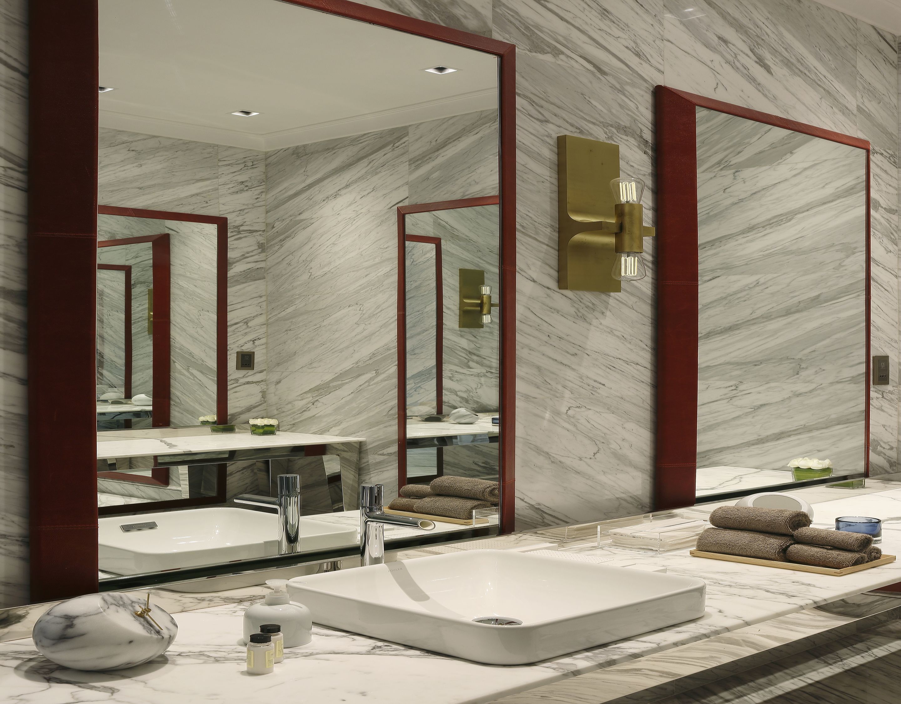 A modern bathroom with a large mirror, marble walls, and a white sink.