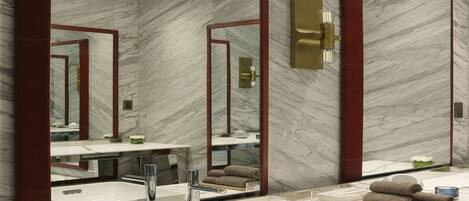A modern bathroom with a large mirror, marble walls, and a white sink.