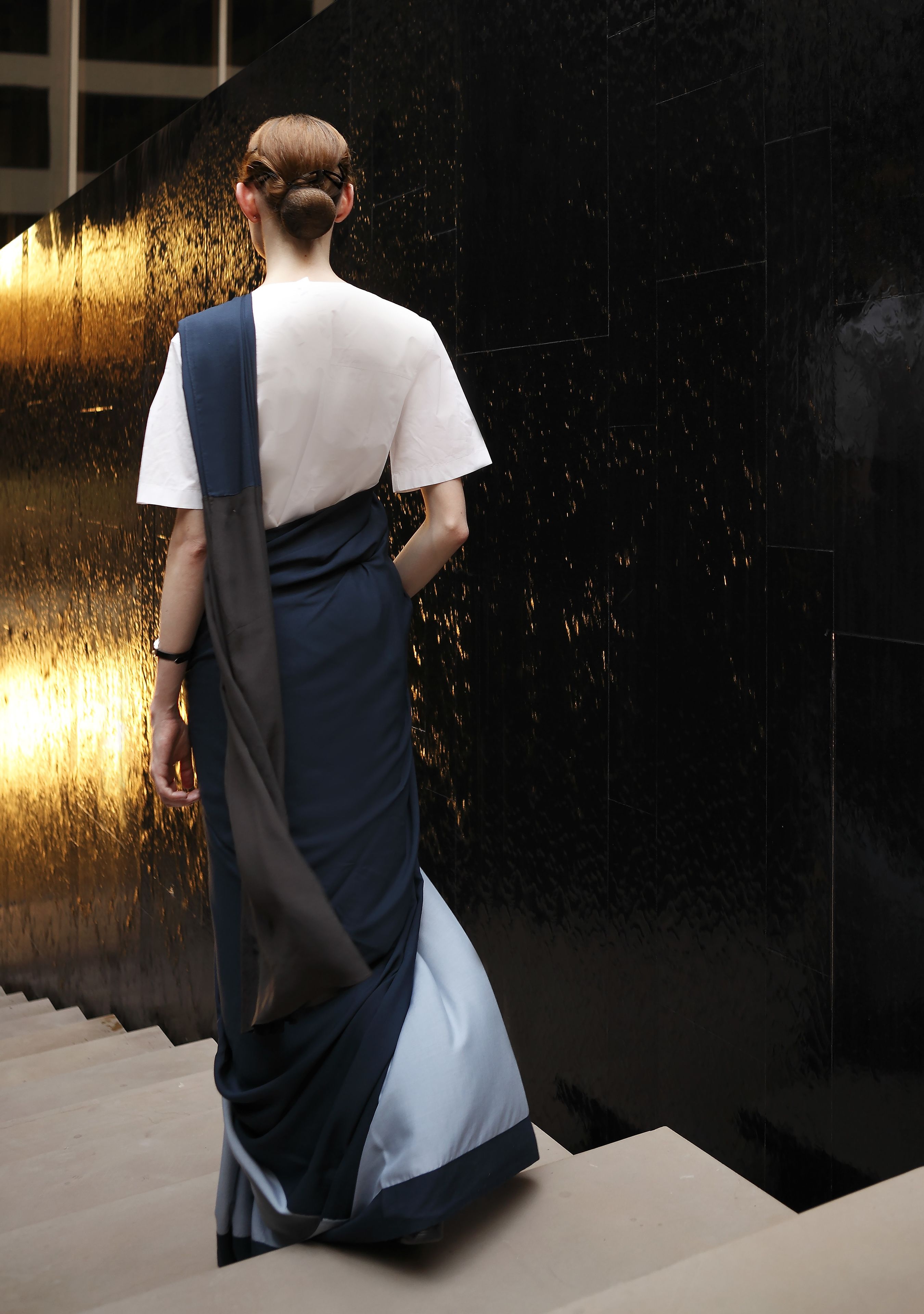 A person in a white top and dark skirt walking on a staircase.