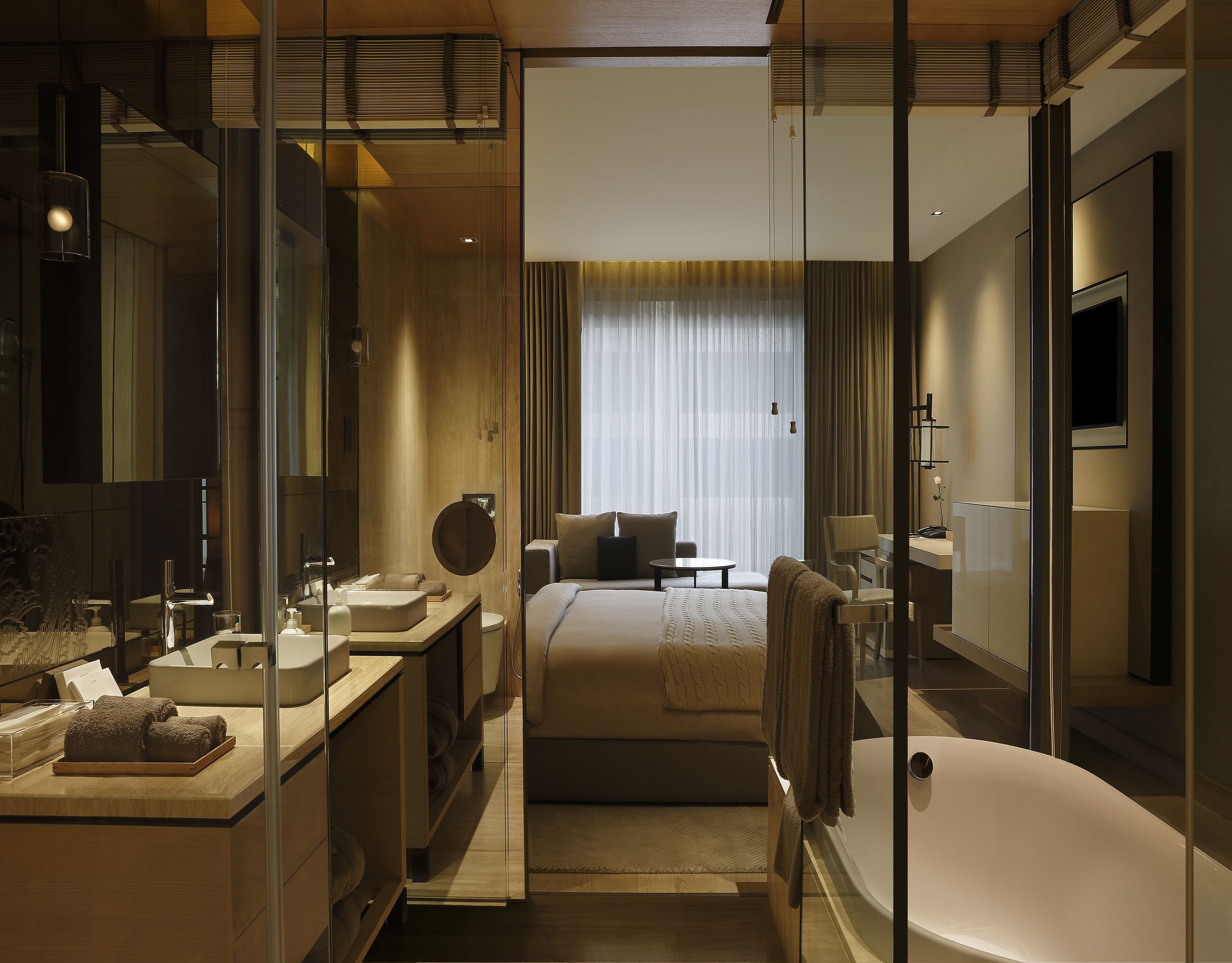 A modern hotel room with a large bed, a sitting area, a desk, a bathtub, and a large window with curtains.