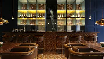 A bar area with leather chairs, a central bar counter, and shelves stocked with bottles.