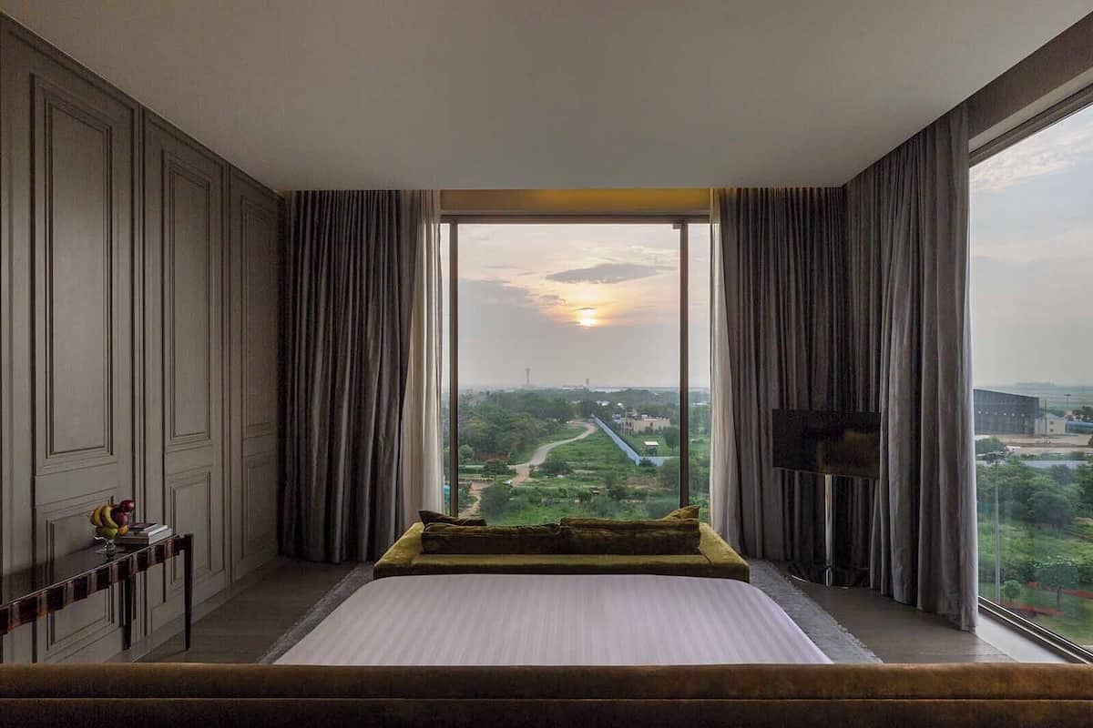 A bedroom with a large bed, a TV mounted on the wall, and a view of a landscape through a large window.