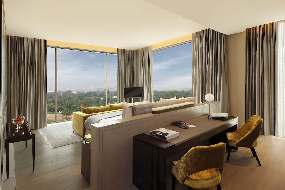 A modern hotel room with a large window, a sofa, a desk, and two chairs.