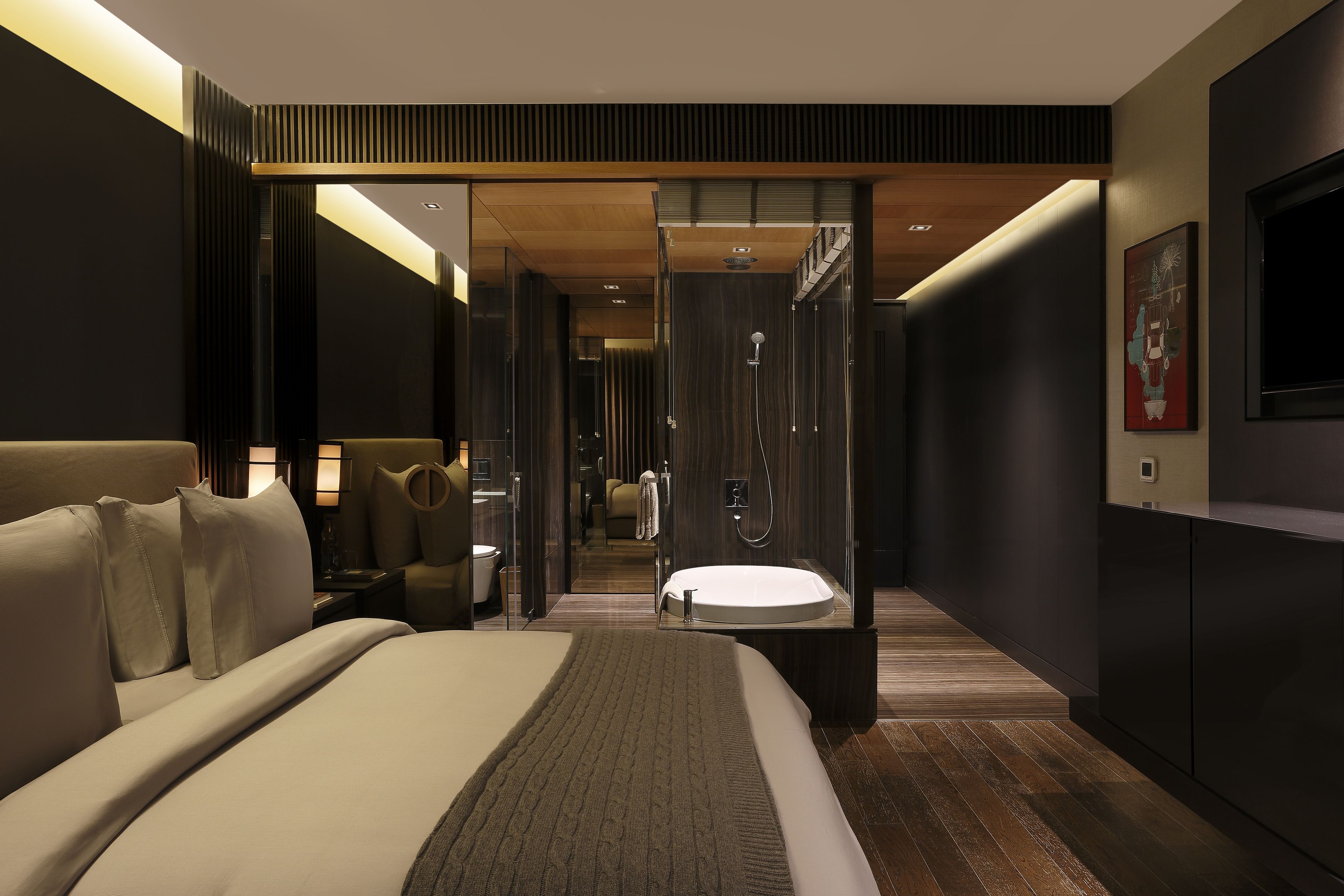 A modern hotel room with a large bed, a bathroom with a bathtub, and a television on the wall.