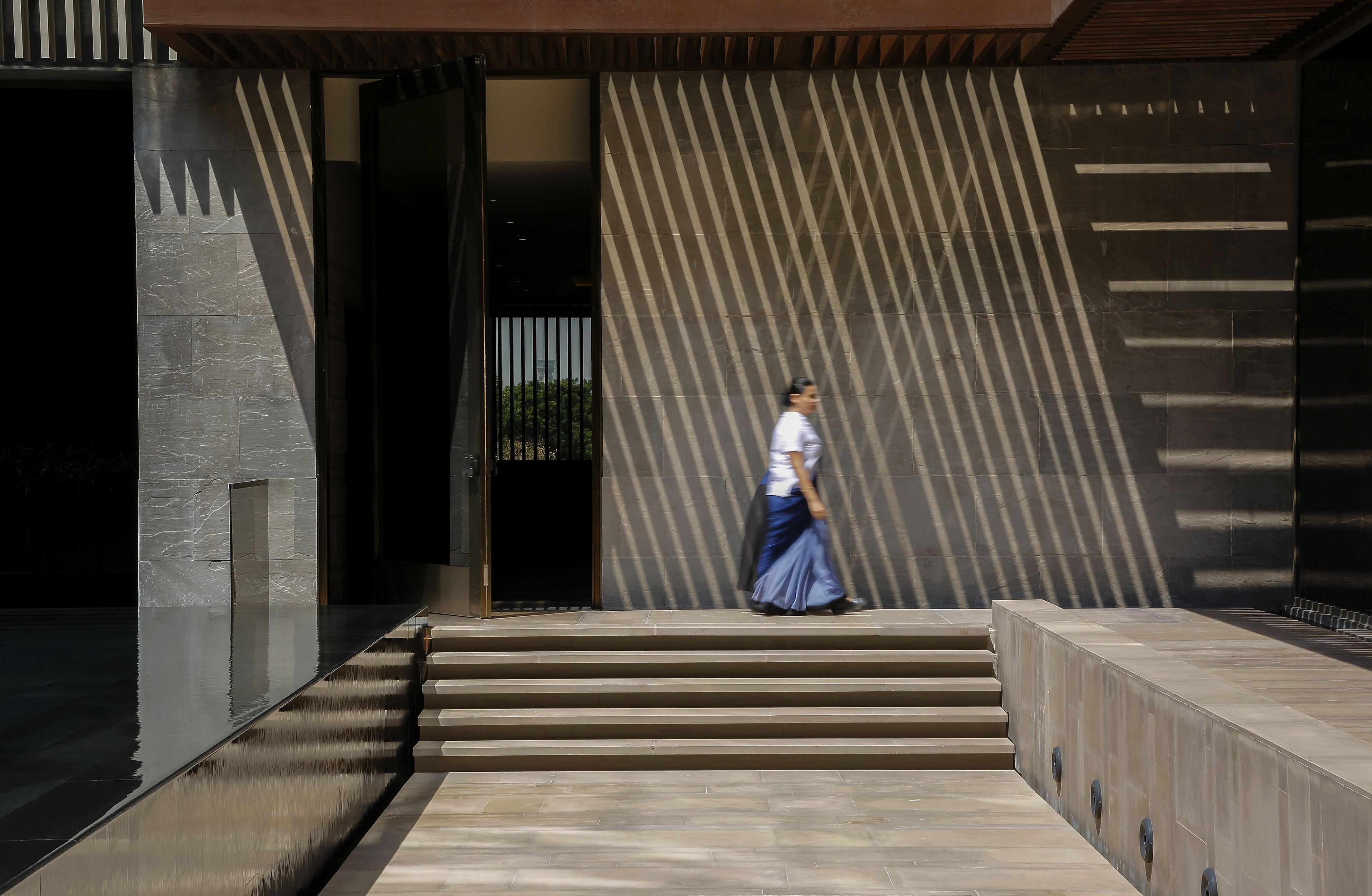 Entrada de um edifício moderno com fachada geométrica e uma pessoa caminhando pelas escadas.