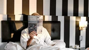 Una persona leyendo un libro en una habitación de hotel con un cabecero a rayas y una mesita de noche con una taza.