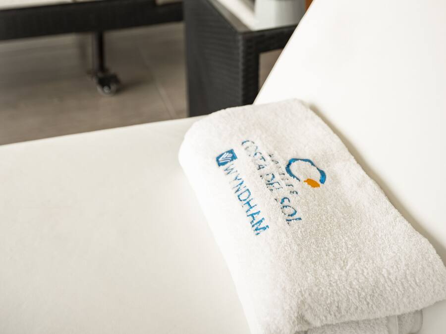 Una habitación de hotel con una cama, una mesita de noche con una planta y una toalla con texto.