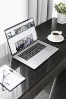 Una laptop sobre una encimera negra, con una taza de café y un par de gafas al lado.