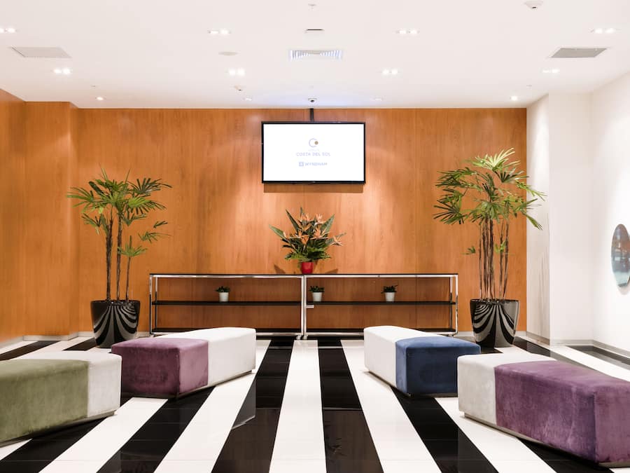 A modern lobby with a black and white striped floor, wooden panel walls, and a central reception desk with a digital screen.