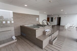 A modern bathroom with a large bathtub, a glass shower enclosure, and a seating area with white chairs.