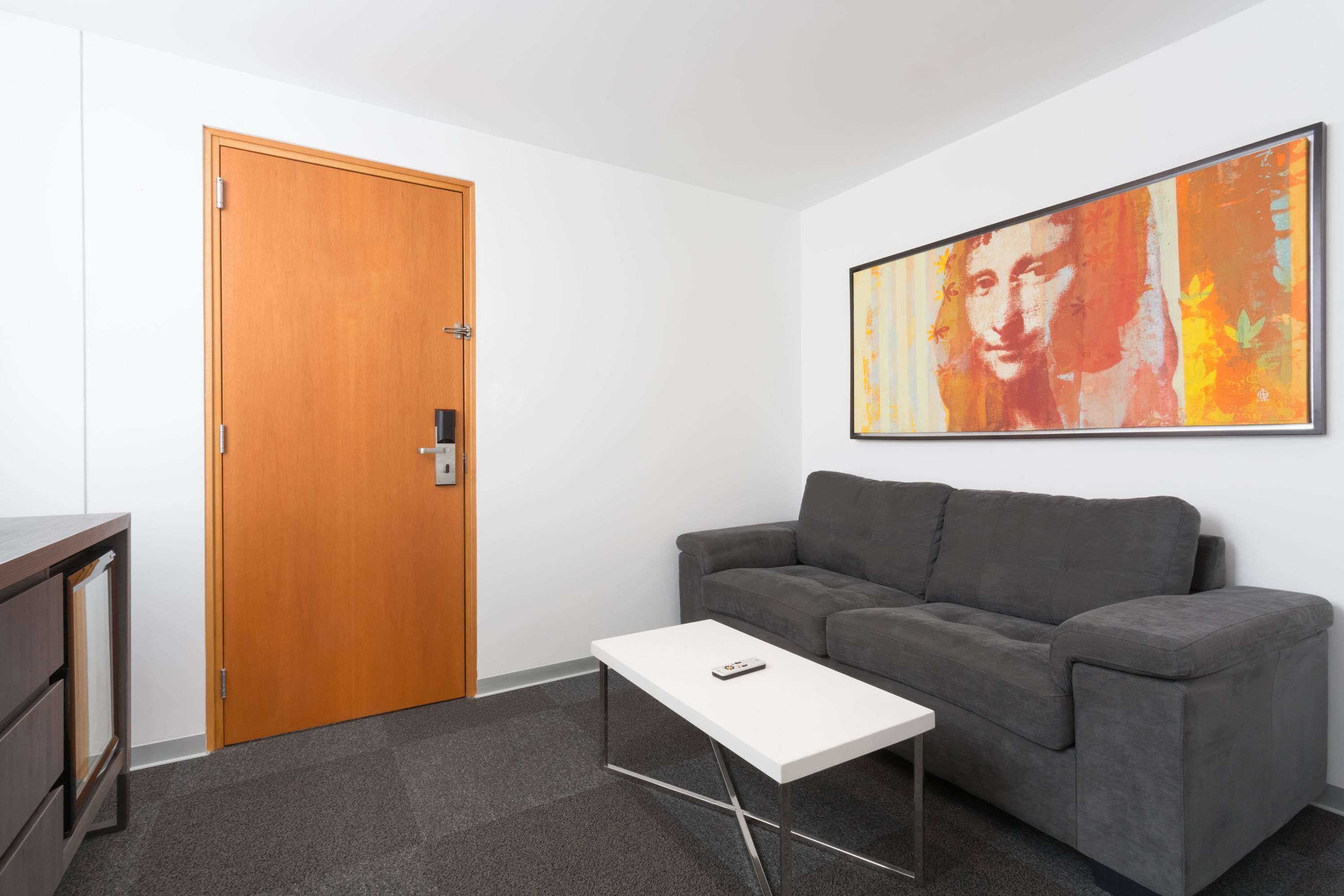 A room with a grey sofa, a white coffee table, a wooden door, and a framed artwork on the wall.