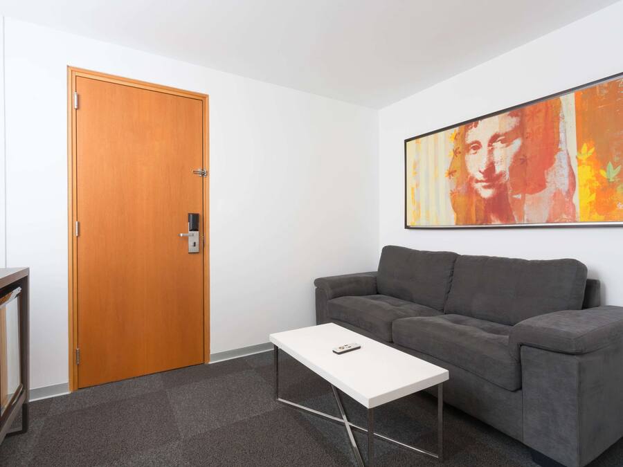 A room with a grey sofa, a white coffee table, a wooden door, and a framed artwork on the wall.