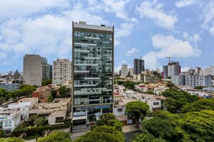 Un edificio moderno de gran altura con fachada de vidrio, rodeado de otros edificios y vegetación.