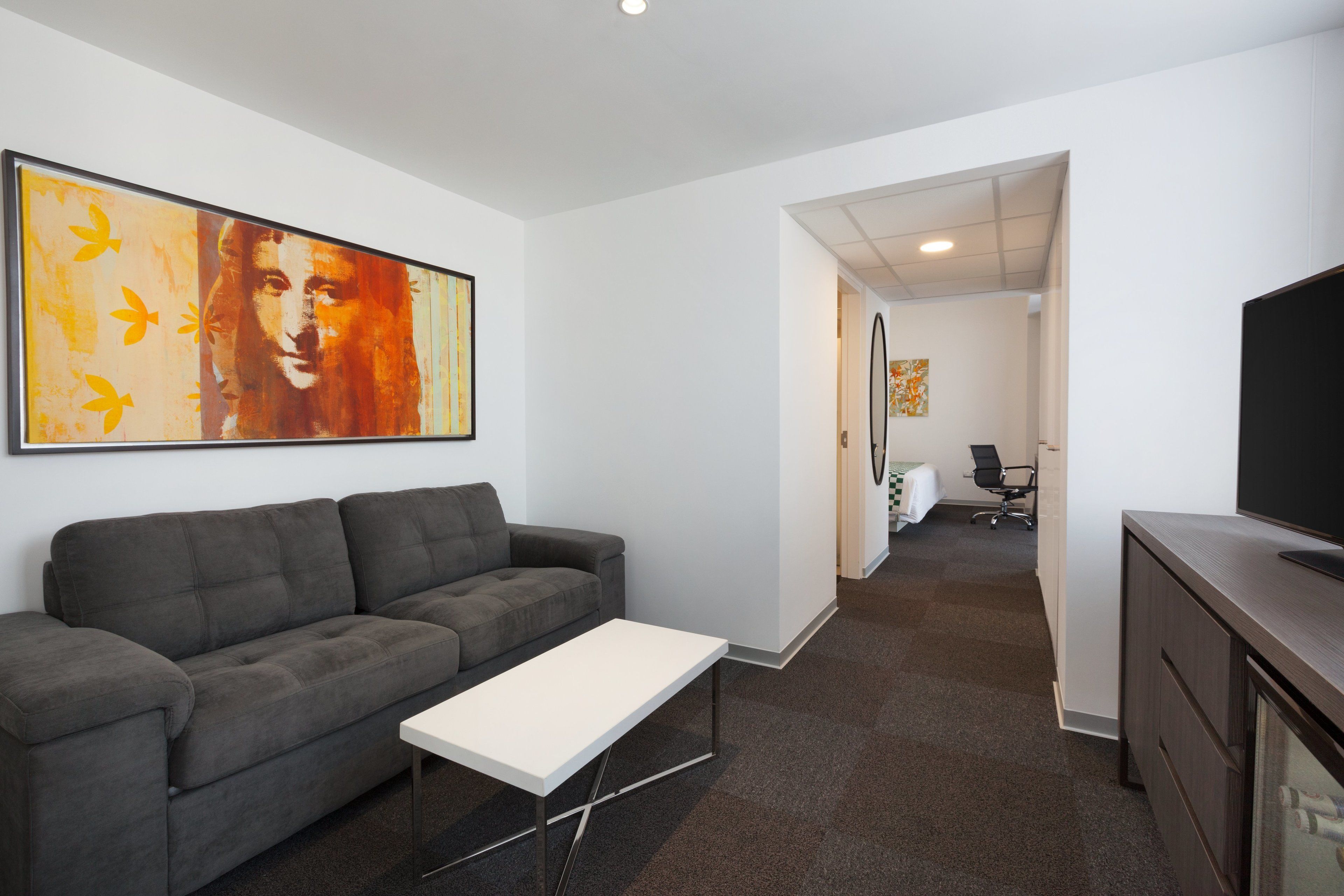 A modern living room with a grey sofa, a white coffee table, and a large abstract painting on the wall.