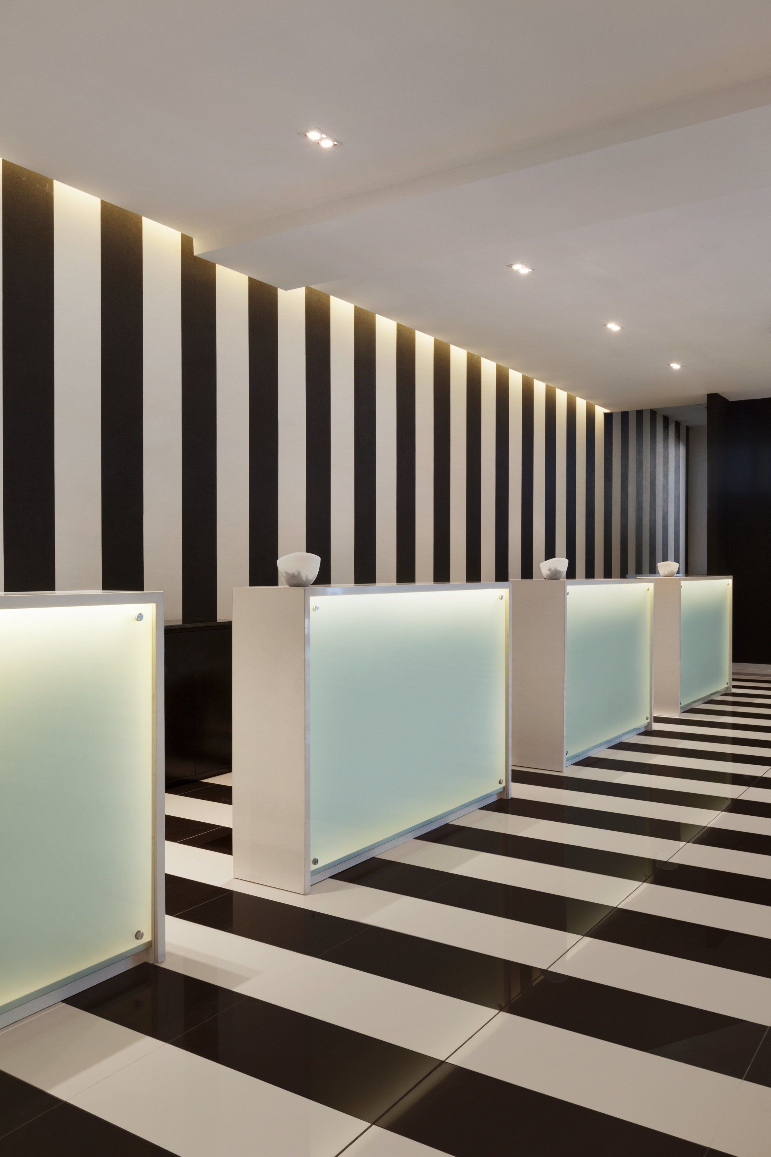 Un espace d’accueil moderne avec un mur à rayures noires et blanches, un sol à carreaux et une rangée de comptoirs d’accueil.