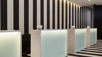 Un espace d’accueil moderne avec un mur à rayures noires et blanches, un sol à carreaux et une rangée de comptoirs d’accueil.