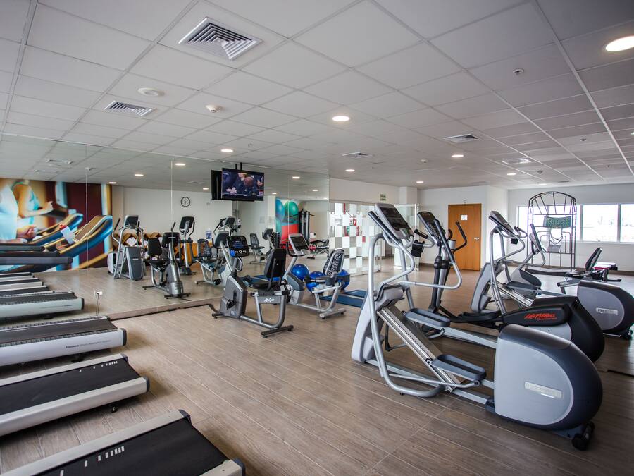 Un gimnasio con cintas de correr, elípticas y bicicletas estáticas.