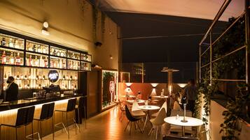 Un área de bar al aire libre con mostrador, asientos y vista de la ciudad de noche.