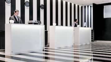 Zona de recepción con dos mostradores, paredes a rayas negras y blancas y relojes que marcan diferentes zonas horarias.