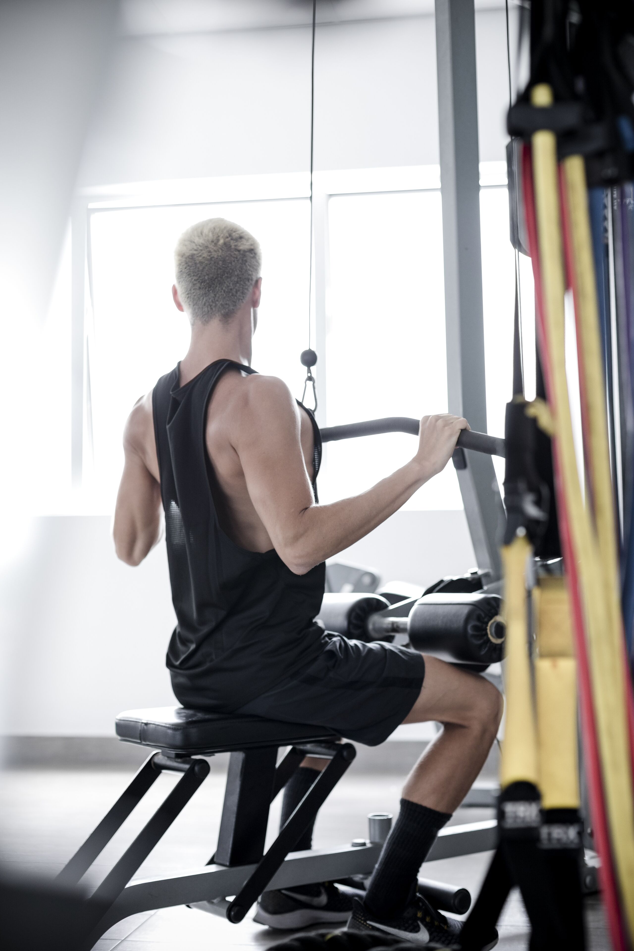 Una persona usando una máquina de remo en un gimnasio con ventanas amplias y equipo de ejercicio.