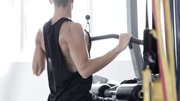 Una persona usando una máquina de remo en un gimnasio con ventanas amplias y equipo de ejercicio.