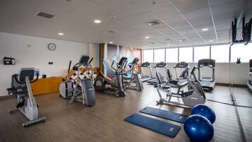 Un gimnasio con diferentes máquinas de cardio, pelotas de ejercicio y colchonetas.
