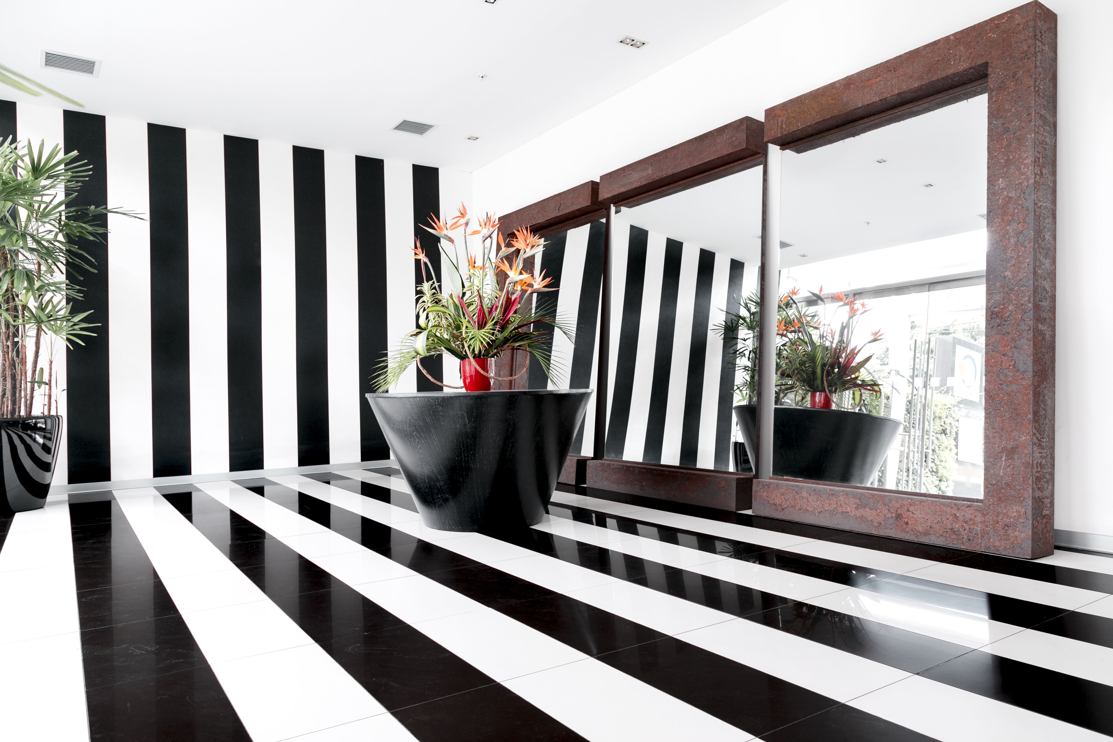 A modern lobby with black and white striped walls, a large mirror, and a central black planter with flowers.