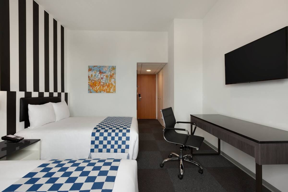 Una habitación de hotel con una cama, un escritorio, una silla y un televisor en la pared.