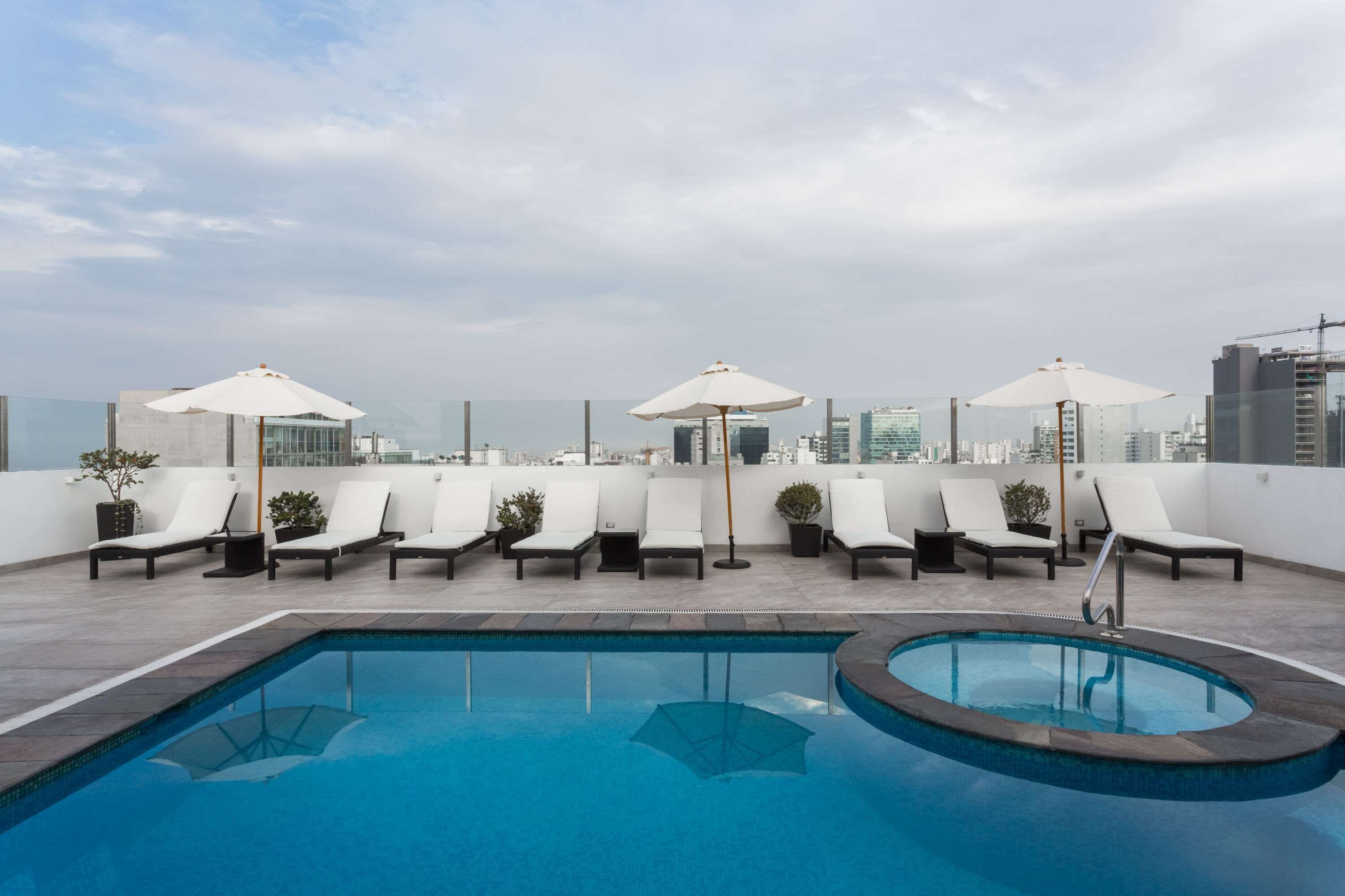 A rooftop pool area with lounge chairs and umbrellas, surrounded by city buildings.