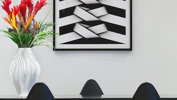 Un interior moderno con una pared blanca, una obra de arte abstracta enmarcada, un jarrón blanco con flores rojas y tres sillas negras.