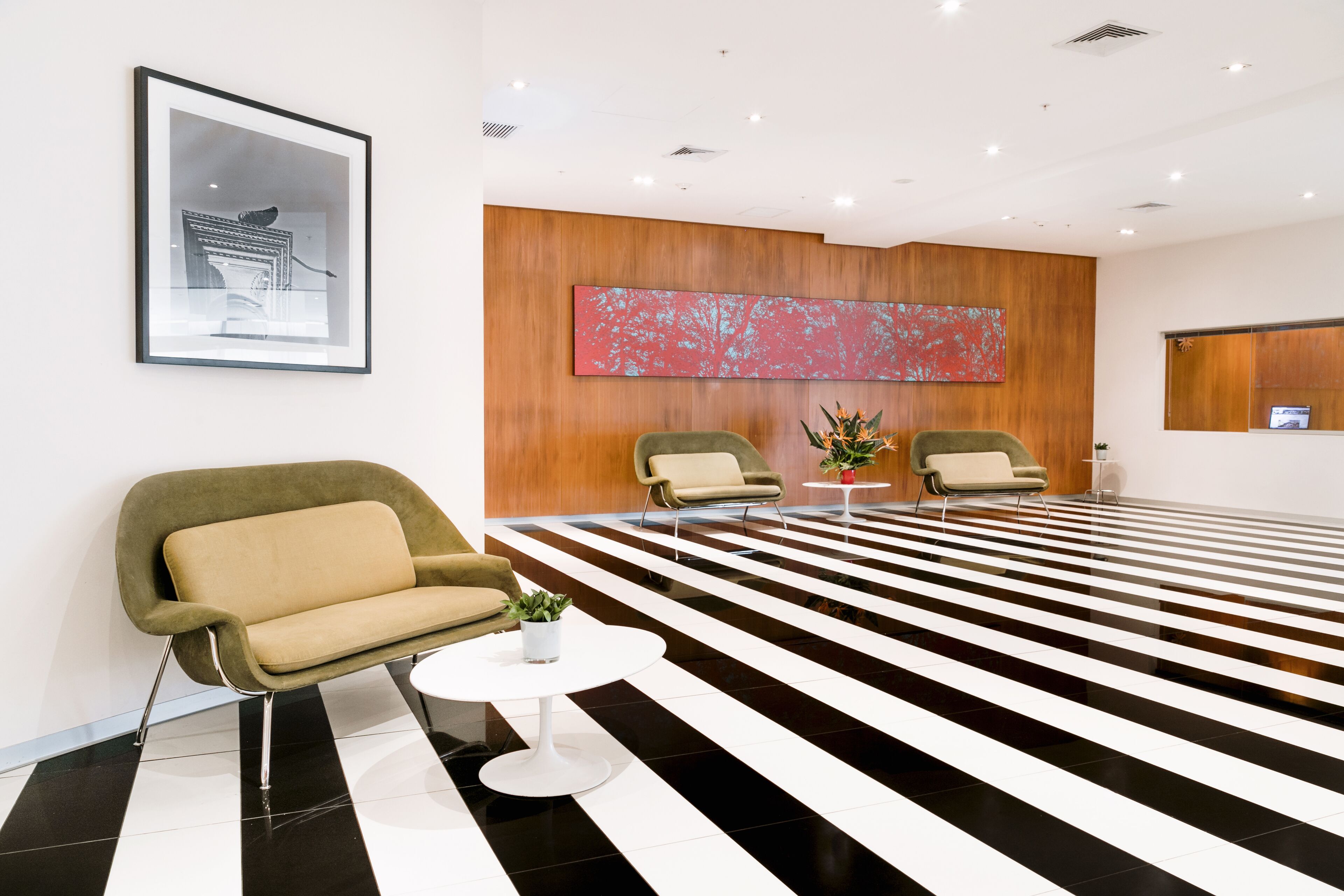 Eine moderne Lobby mit einem schwarz-weiß gestreiften Boden, zwei grünen Sessel, einem weißen runden Tisch mit Pflanze und einem großen abstrakten Gemälde an der Wand.