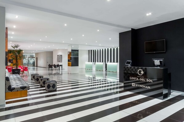 Un vestíbulo de hotel con mostrador de recepción, mostradores de registro y zonas de estar.