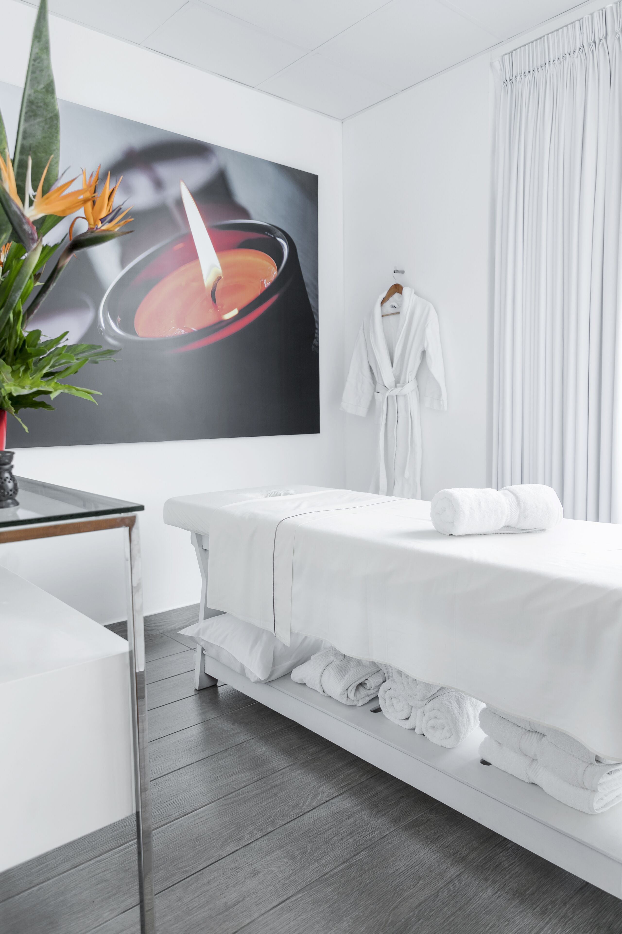 Een moderne spa-ruimte met een massagetafel, een witte badjas en een groot kunstwerk van een kaars.