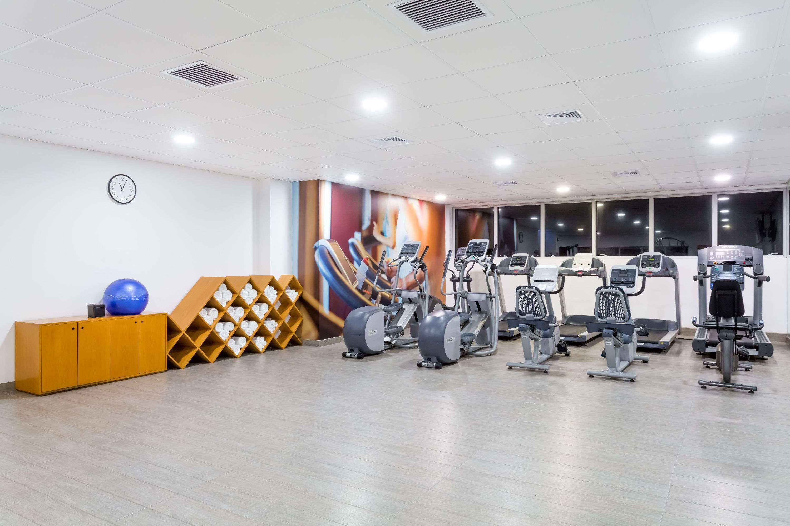 Een fitnessruimte met trainingsapparatuur, een klok en een muur met een kleurrijke muurschildering.