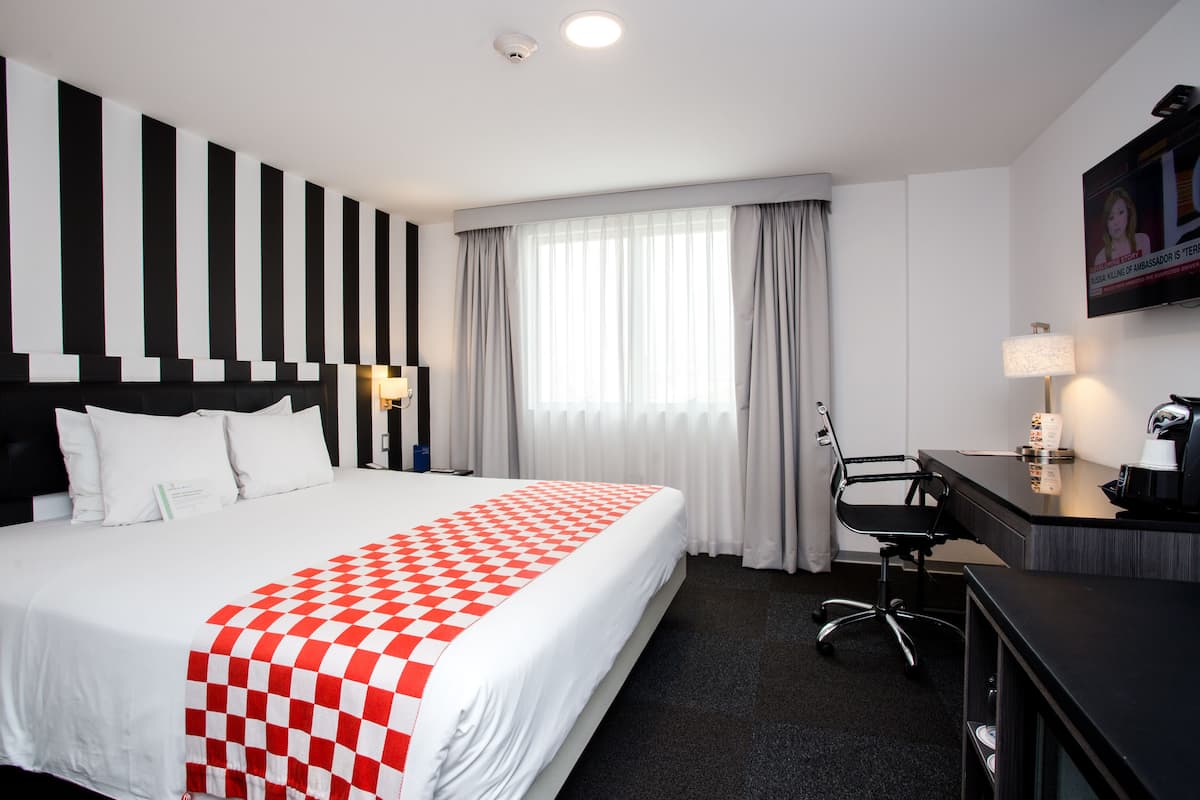 Una habitación de hotel con una cama grande, un escritorio, una silla, un televisor y una ventana con cortinas.