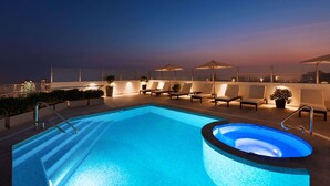 Piscina en la azotea con sillones de descanso y sombrillas, con vistas a la ciudad.