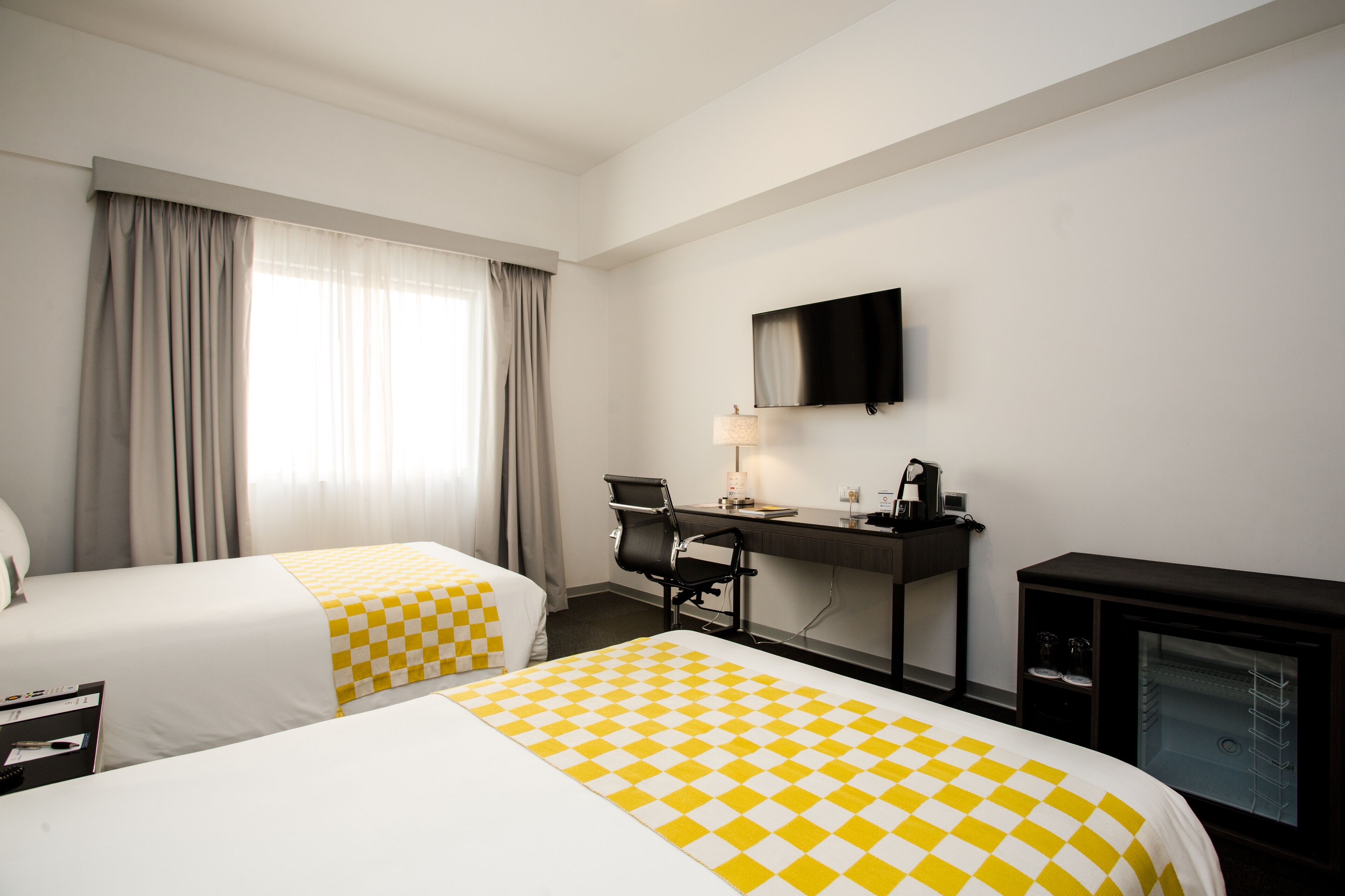 Habitación de hotel con dos camas, un escritorio, una silla, un televisor y un minibar.