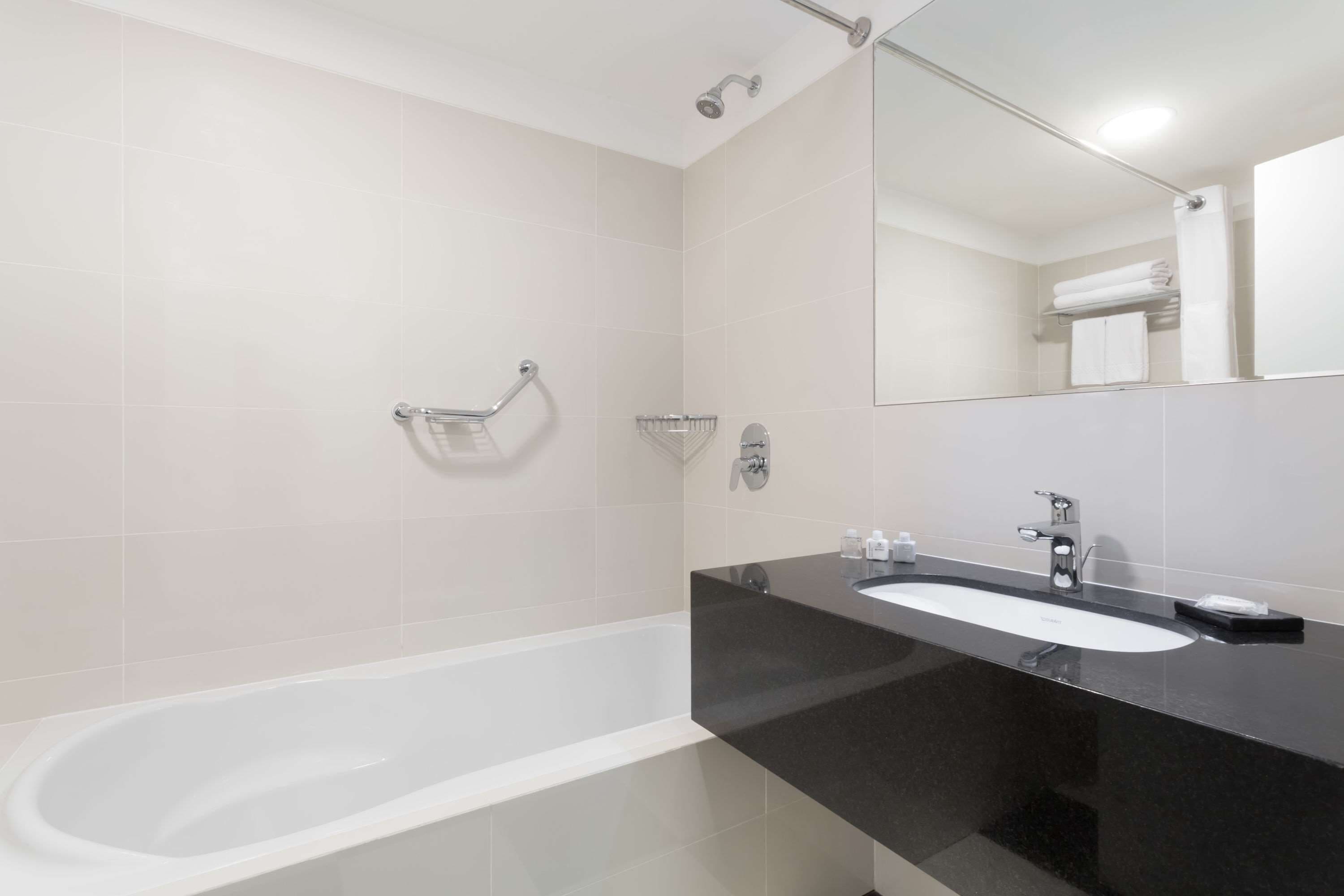 A modern bathroom with a white bathtub, a black sink, and a large mirror.
