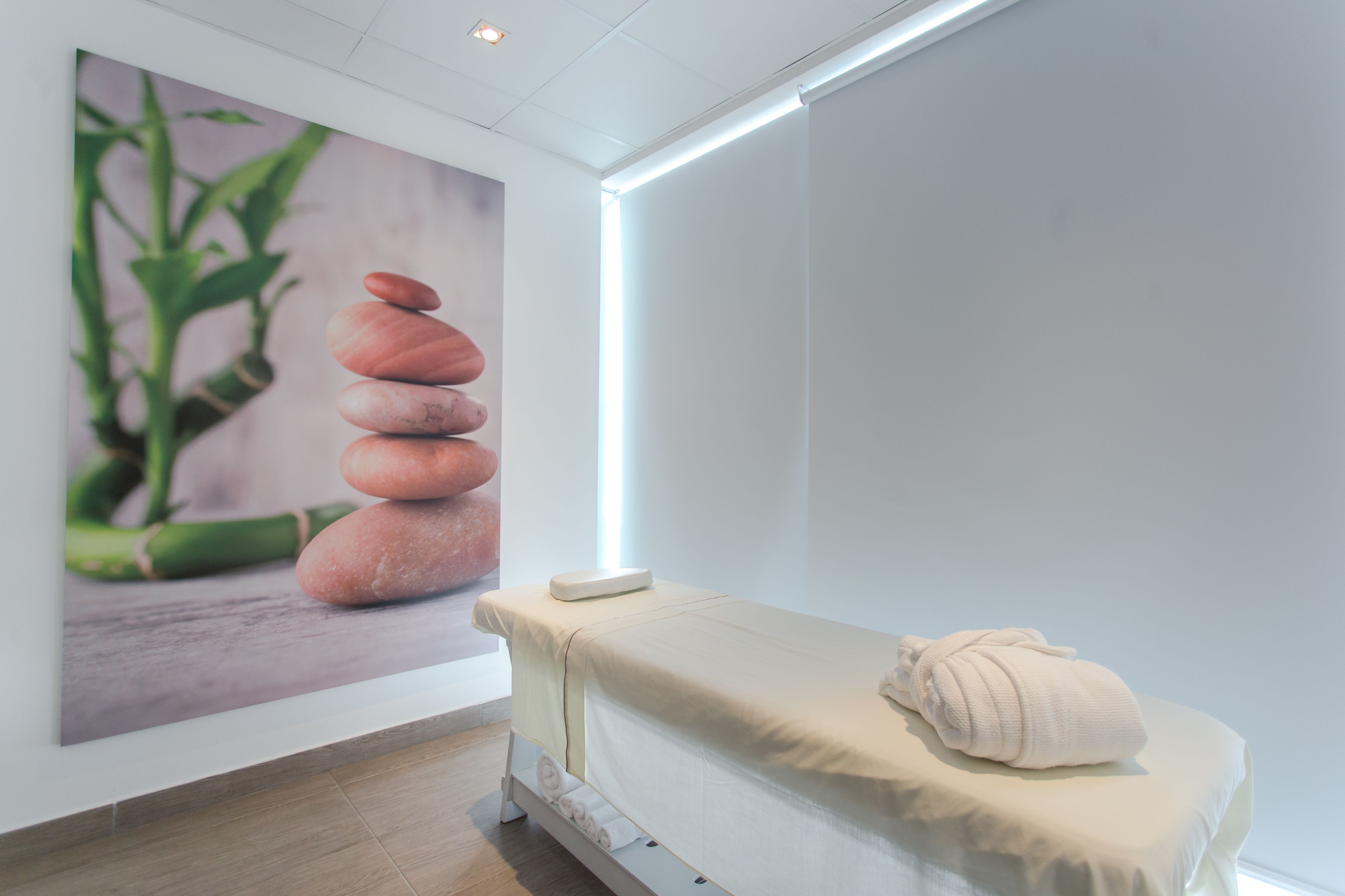 A spa room with a massage table, a poster of stones and bamboo, and a ceiling light.