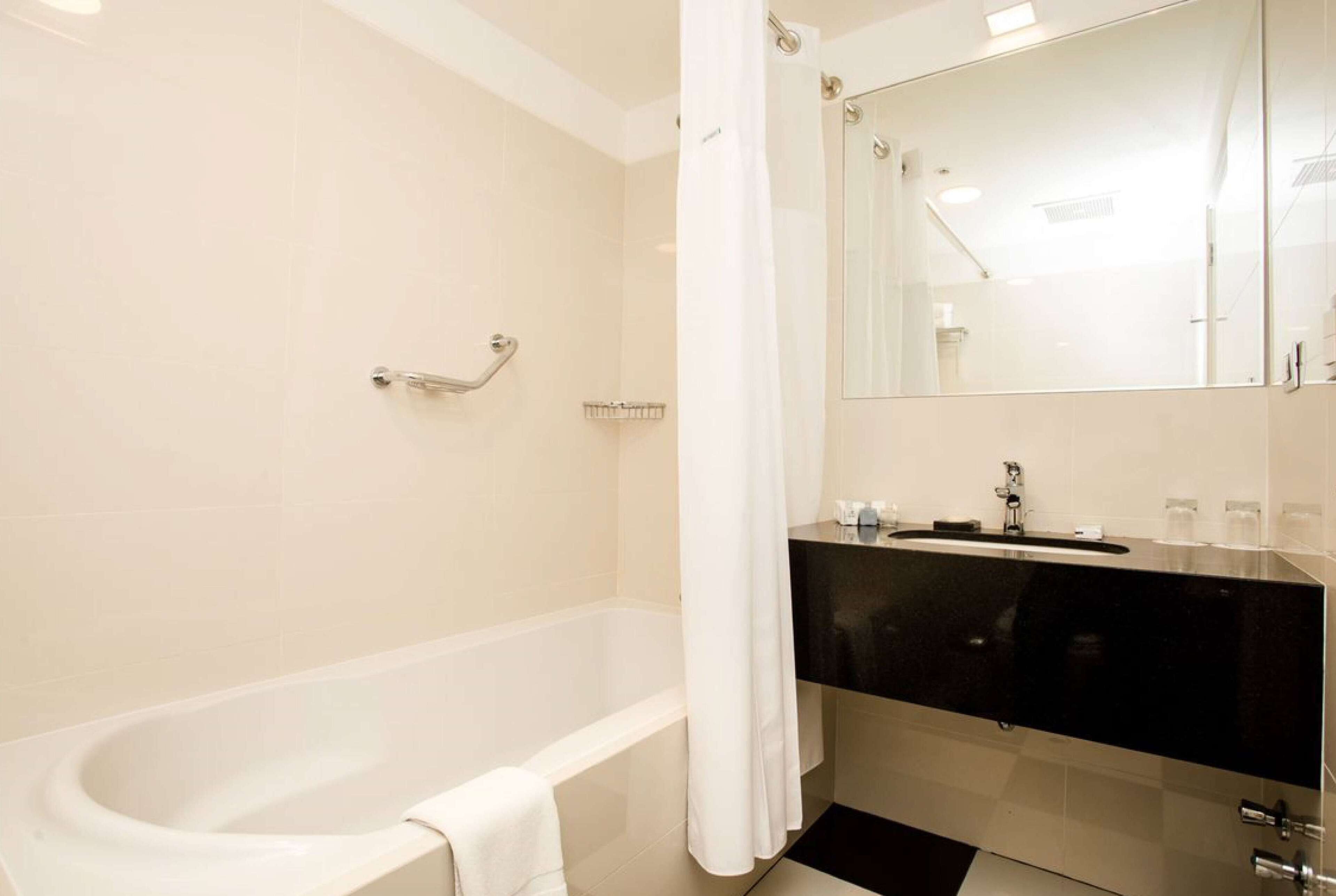 Un baño moderno con una bañera, un mueble de tocador negro y un espejo grande.