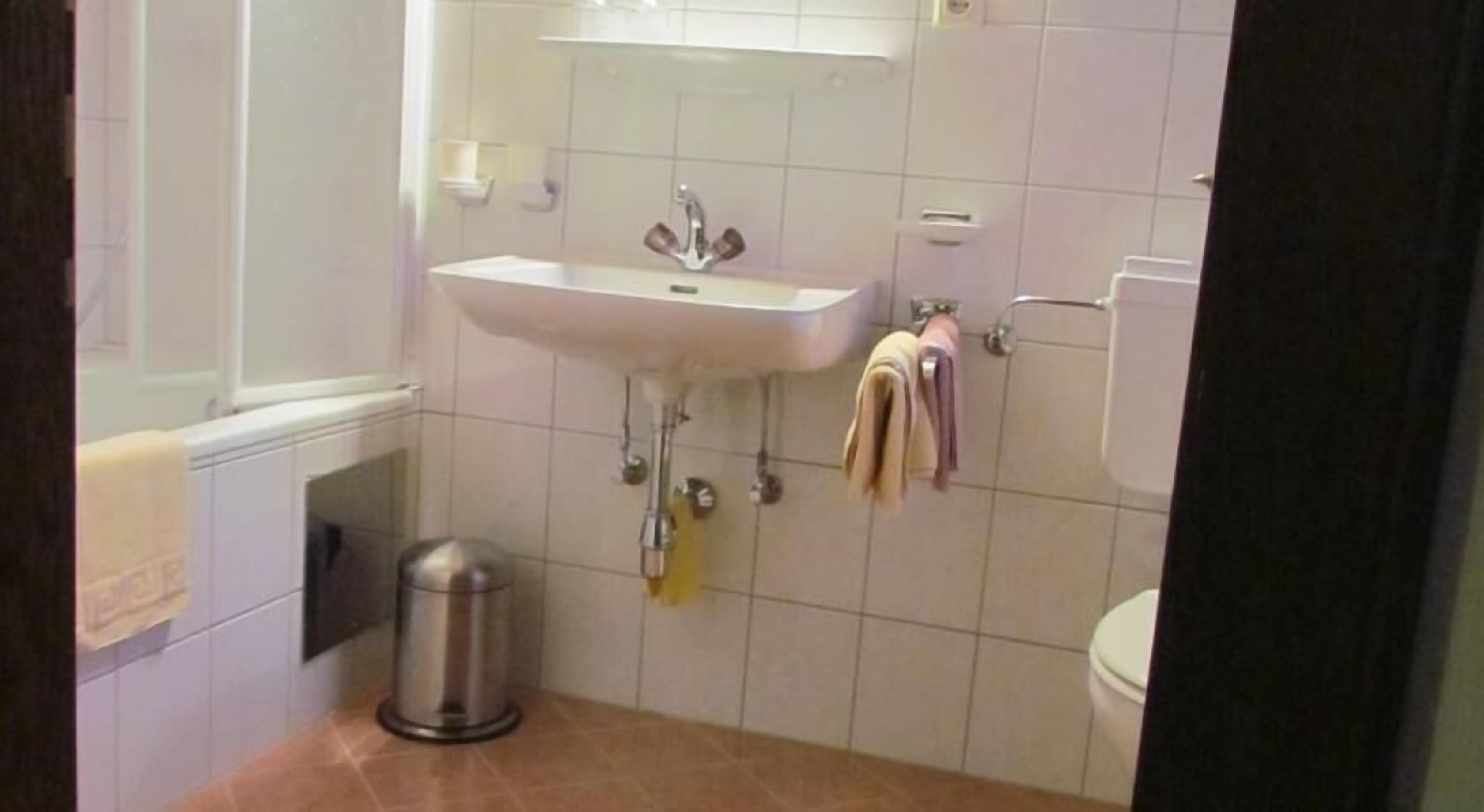 A bathroom with a sink, mirror, and toilet. There is a towel rack with towels hanging on it.