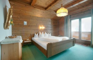 A wooden-paneled bedroom with a bed, a nightstand, a lamp, and a window with a view. - Gästehaus Auer (Thiersee)
