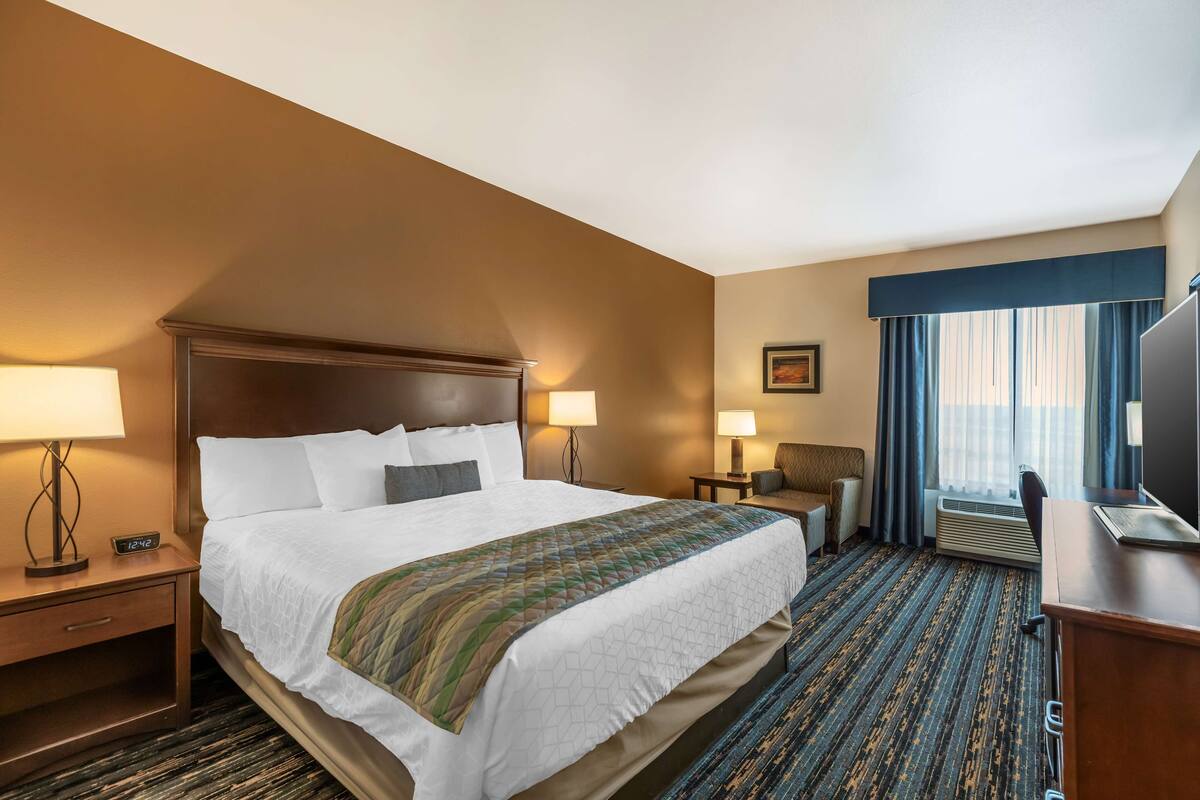 A hotel room with a large bed, bedside tables with lamps, a desk, and a television.
