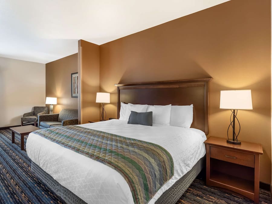 A hotel room with a large bed, two bedside lamps, a nightstand, a chair, and a carpeted floor.