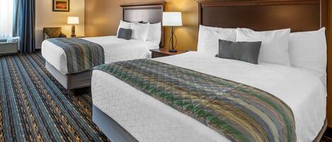 A hotel room with two beds, a large window with curtains, a wall-mounted lamp, and a patterned carpet.